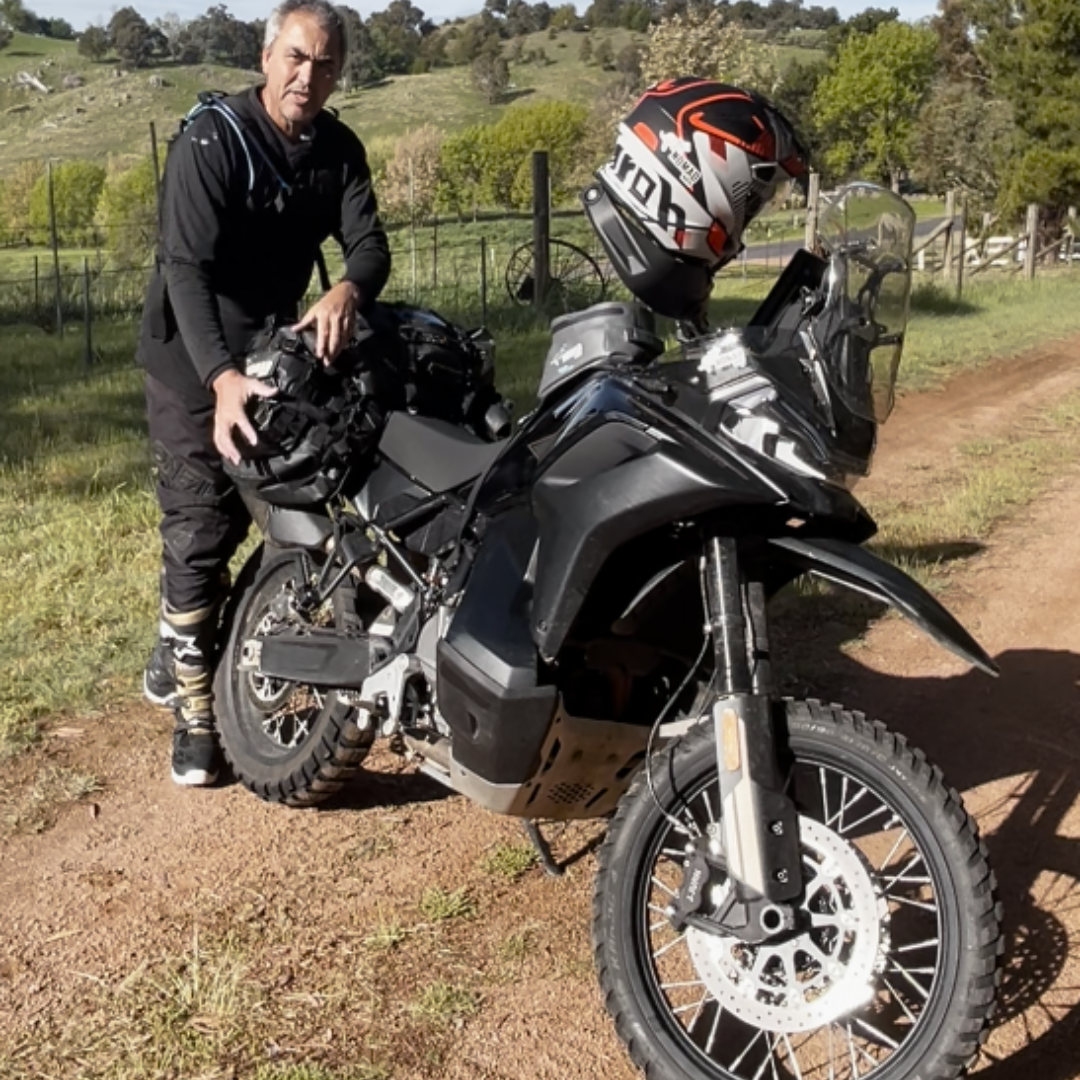 Man with a motorcycle and helmets on a dirt road in a rural setting